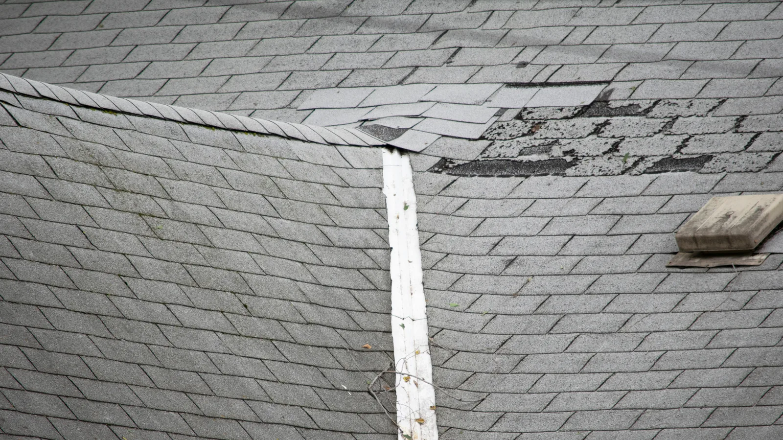Creased and broken shingle tabs on a weathered gray roof